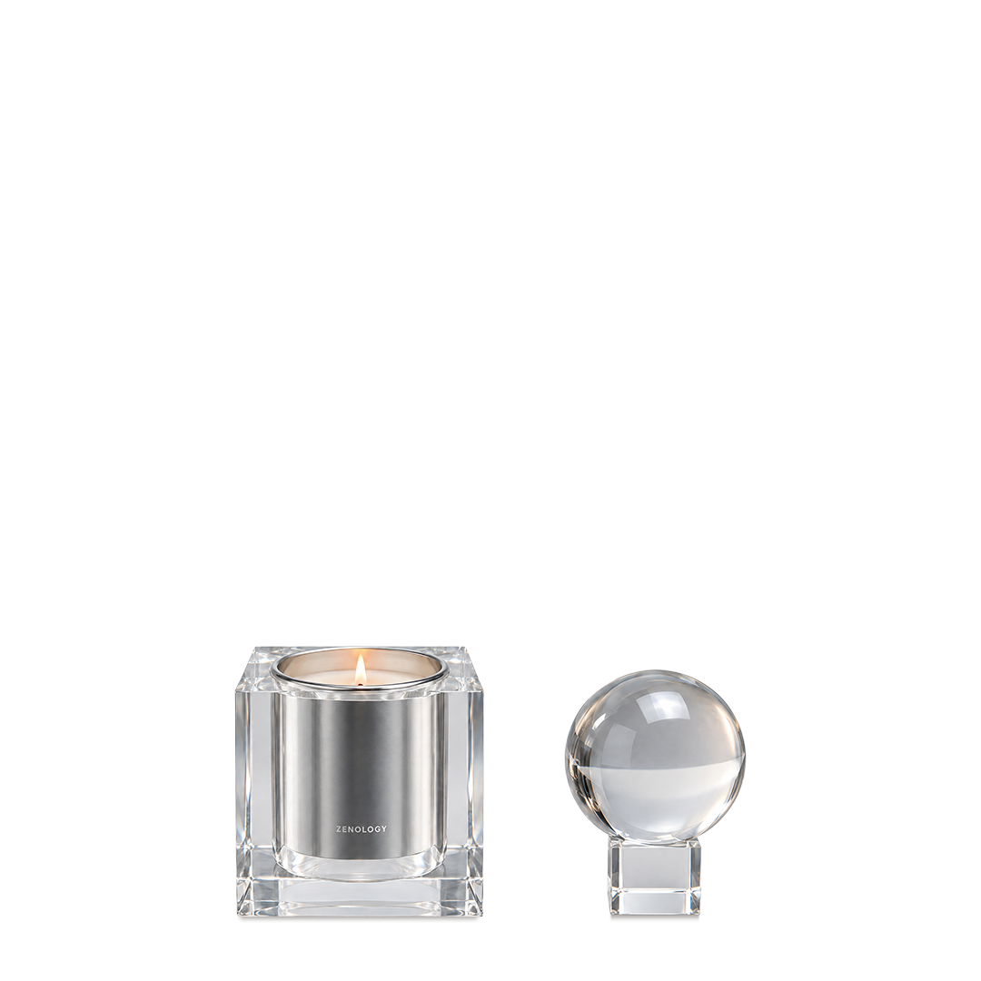 Zenology Crystal Candle Holder i klar kristall med tänt ljus och klotformat lock på ett litet kubstöd.